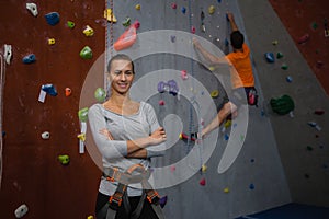 Portrait of confident athlete standing against man climbing wall in club