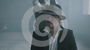 Portrait confident bad man sit on chair in fedora hat and other man walking from behind with a gun and shoot him in the
