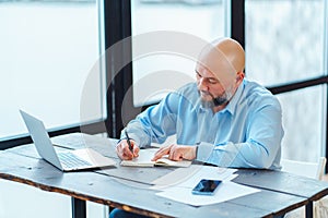 Portrait of confident bald man,sitting table in office, signing contract, brainstorming. Working finance business.