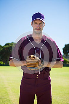 Portrait of confident baseball pitcher standing against sky