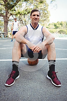 Portrait of confident basketball player sitting on ball