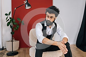 Portrait of confident bearded business man wearing elegant formalwear sitting on chair with crossed arms, serious