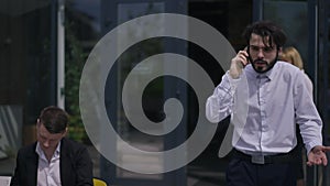 Portrait of confident bearded man persuading partners talking on phone walking in slow motion passing colleagues