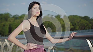 Portrait of confident beautiful Caucasian woman standing on bridge on sunrise and smiling. Charming young brunette girl