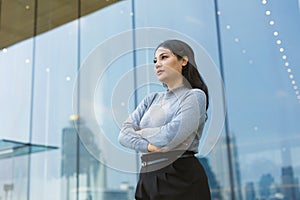 portrait confident business indian women standing againt large glass windows office building arm crossing