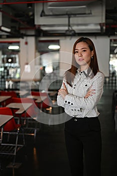 Portrait of confident business woman is standing in meeting room with her arms crossed.