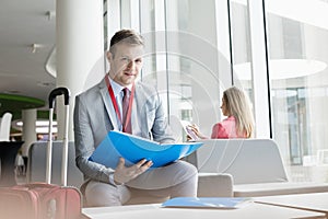 Portrait of confident businessman holding file while sitting at lobby in convention center