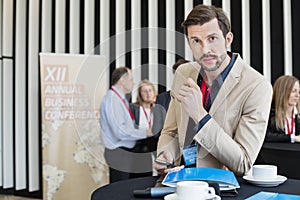 Portrait of confident businessman holding smart phone during coffee break in convention center