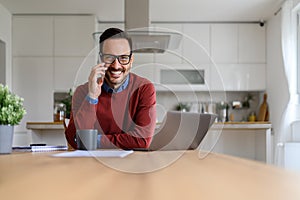 Portrait of confident businessman making business call over cellphone while using laptop at home