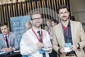 Portrait of confident businessmen holding coffee cups at lobby in convention center