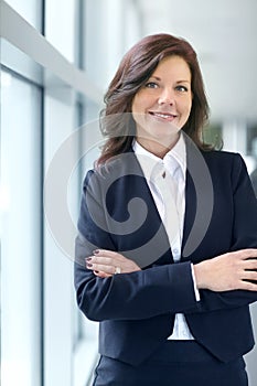 Portrait of a confident businesswoman with arms crossed in a modern office. One smiling professional entrepreneur