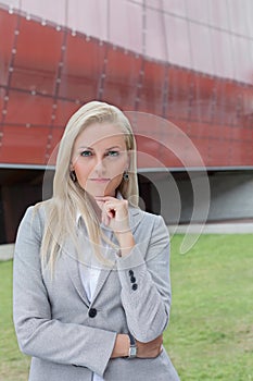 Portrait of confident businesswoman standing with hand on chin against office building