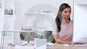 Portrait of confident call center agent wearing headset and sending email in modern office. Young professional woman