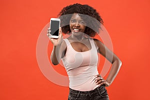 Portrait of a confident casual afro girl showing blank screen mobile phone isolated over red background