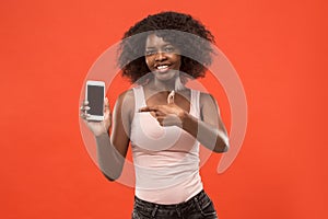 Portrait of a confident casual afro girl showing blank screen mobile phone isolated over red background