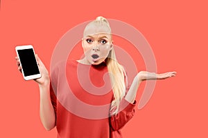 Portrait of a confident casual girl showing blank screen mobile phone isolated over coral background