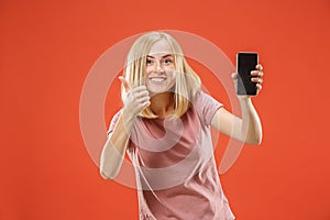 Portrait of a confident casual girl showing blank screen mobile phone isolated over red background