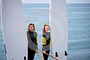 Portrait of confident caucasian man and woman sup paddleboarders , posing on beach photo
