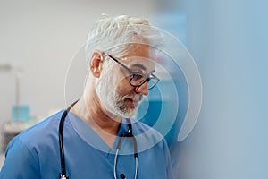 Portrait of confident ER doctor standing in hospital emergency room. Handsome doctor in scrubs standing in modern