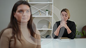 Portrait of confident expert female therapist talking to blurred woman sitting at front at table. Beautiful professional