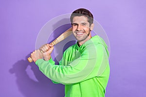 Portrait of confident fearless dangerous guy with brunet hairdo green hoodie hold baseball bat isolated on violet color