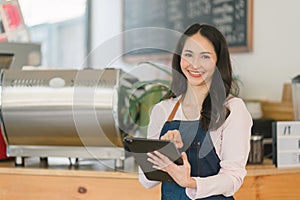 Portrait of confident female barista standing at counter. Woman cafe owner in apron looking at camera and smiling while