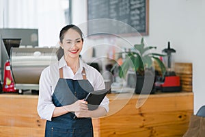 Portrait of confident female barista standing at counter. Woman cafe owner in apron looking at camera and smiling while