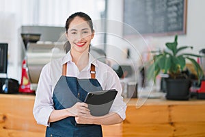 Portrait of confident female barista standing at counter. Woman cafe owner in apron looking at camera and smiling while