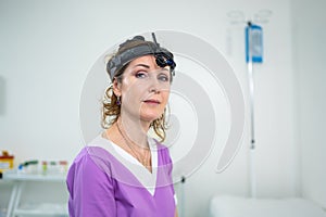 Portrait of confident female doctor. Female ENT doctor in purple medical clothes posing in office of the clinic on her