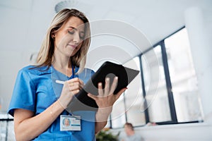 Portrait of confident female doctor standing in Hospital corridor. Beautiful nurse wearing blue scrubs, holding