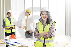 Portrait of confident female engineer standing on frontage while colleagues discussing and meeting on background