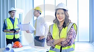 Portrait of confident female engineer standing on frontage while colleagues discussing and meeting on background