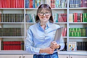 Portrait of confident female teacher holding laptop inside library