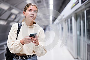 Portrait of a confident girl in the subway, holding a mobile phone photo