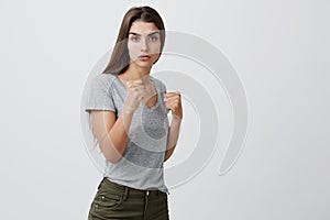 Portrait of confident good-looking young caucasian girl with dark long hair in gray t-shirt and brown jeans standing in