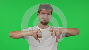 Portrait of confident guy is showing thumbs down gesture. Green screen