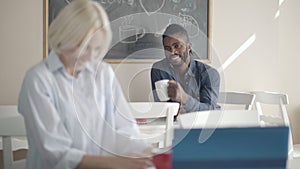 Portrait of confident handsome African American man smiling to blurred blond Caucasian woman looking at him in lunchroom