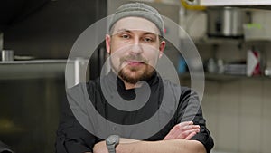 Portrait of a confident and happy chef with a beard in a black uniform in the kitchen in a restaurant. Joyful Chief in a