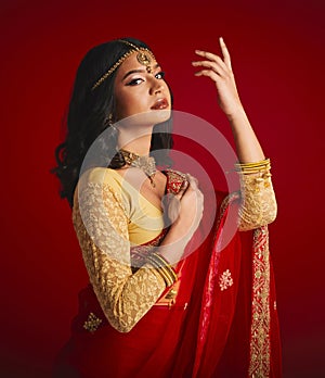 Portrait, confident and Indian woman with fashion, traditional dress and beauty against a red studio background. Face