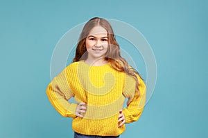 Portrait of confident little girl standing with hands on hips and looking at camera with smile.