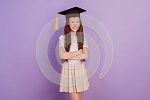 Portrait of confident little girl wear student hat crossed hands on purple background