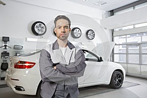 Portrait of confident male automobile mechanic standing in front of car at workshop