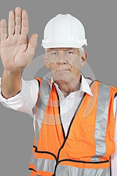 Portrait of confident male construction worker with stop gesture over gray background