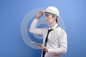 Portrait of confident male engineer wearing a white helmet  using tablet over blue  background studio