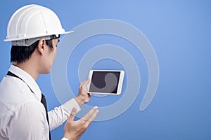 Portrait of confident male engineer wearing a white helmet  using tablet over blue  background studio