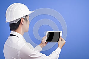 Portrait of confident male engineer wearing a white using tablet over blue background studio