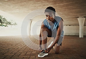 Portrait of a confident male jogger tying his shoelaces on pavement under the bridge