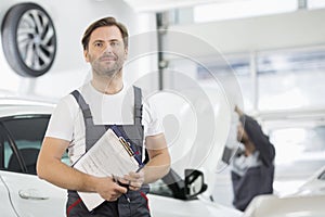 Portrait of confident male maintenance engineer with clipboard in car repair shop