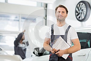 Portrait of confident male maintenance engineer with clipboard in car repair shop