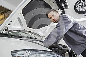 Portrait of confident male repair worker repairing car engine in repair shop